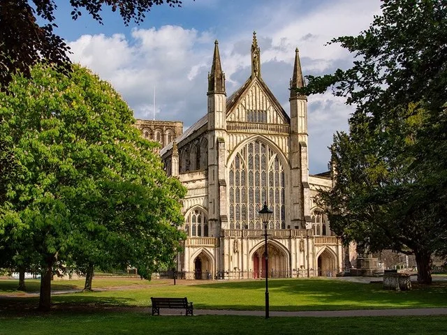 Winchester Cathedral stands tall surrounded by green trees.