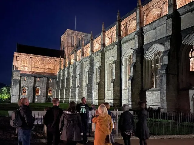 People standing outside Winchester Cathedral illuminated at night.