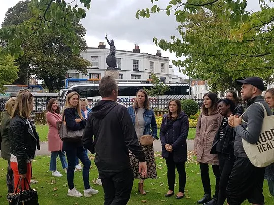 A group of people stand in a park near a statue.